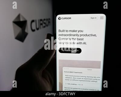 In this photo illustration, a person is holding a smartphone with the web page of ai software company Cursor (Anysphere Inc.) on screen in front of logo. Stock Photo