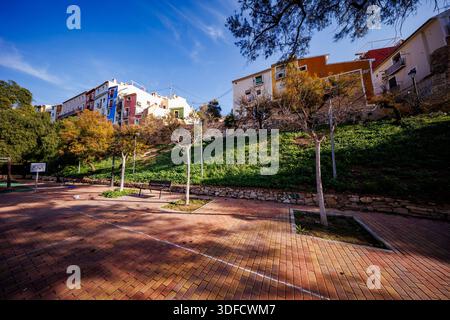 A wide-angle view of a peaceful public park with brick paving and benches, situated beneath the iconic hanging colorful houses and ancient stone walls Stock Photo