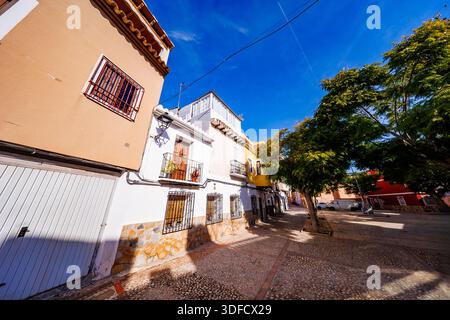 A vibrant street scene showing a mix of white and yellow houses with decorative stone bases, framed by lush green trees under a deep blue sky. Stock Photo