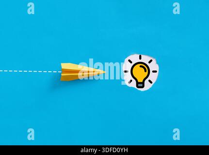 Startup business concept with yellow paper plane following dotted line path towards light bulb on blue background Stock Photo