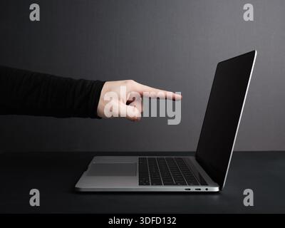 Male hand pointing at modern laptop with blank screen on gray background, ideal for mockups and advertisement Stock Photo