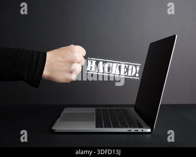 Hacker punching laptop with hacked message appearing, cyber crime and security breach concept Stock Photo