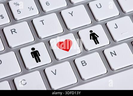 Online dating and love concept is illustrated by a red heart between man and woman icons on keyboard keys Stock Photo