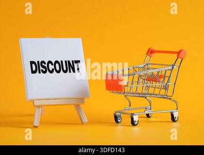 Small shopping cart and canvas showing discount word on bright yellow background representing sales and retail Stock Photo