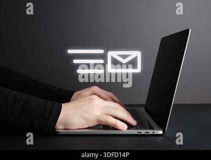 Businessman typing on a laptop keyboard while an email icon hologram hovers above, representing to send an e-mail and online messaging. Stock Photo
