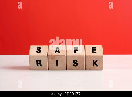 Wooden cubes composing the words risk and safe on a white surface with a red background Stock Photo