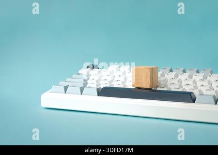 One square wood block on top of computer keyboard, on light blue background. Stock Photo
