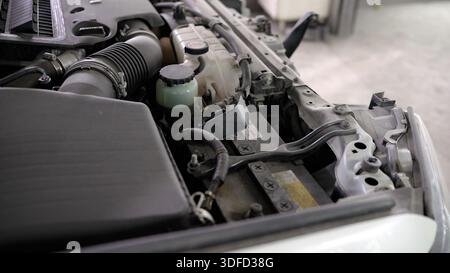 Car engine bay showing internal components like the battery, fluid reservoirs, air intake, and hoses for maintenance Stock Photo
