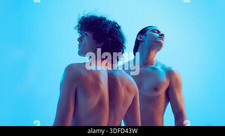 Two young men back view looking upward in blue studio light. Stock Photo
