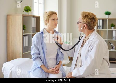 Female physician using stethoscope to examine young patient in clinic room Stock Photo