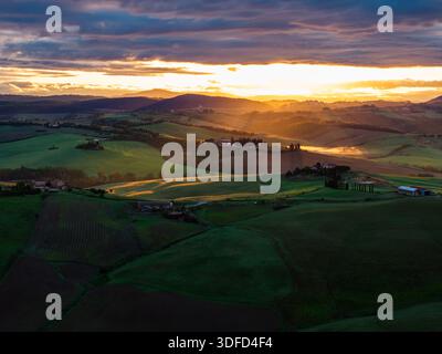 Aerial view of sunbeams piercing through the clouds over the rolling green hills and farms, casting long shadows across the landscape, Crete Senesi, I Stock Photo