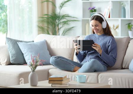 Happy woman using headphone and tablet to watch online streaming videos at home Stock Photo