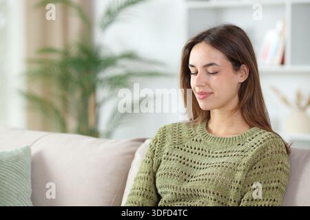 Satisfied woman in green closing eyes meditating sitting on a couch at home Stock Photo