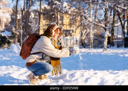 Young woman wearing warm clothes touching fresh snow outdoors in winter Stock Photo