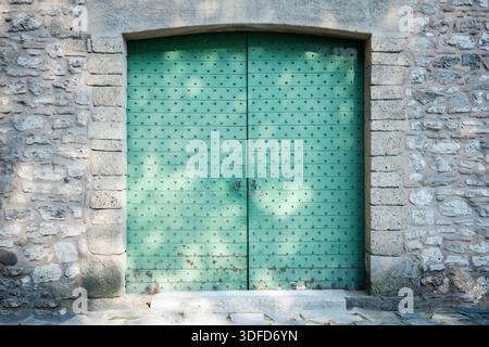 Rustic green studded metal door set in weathered stone wall, reflecting history, security, and traditional architecture Stock Photo