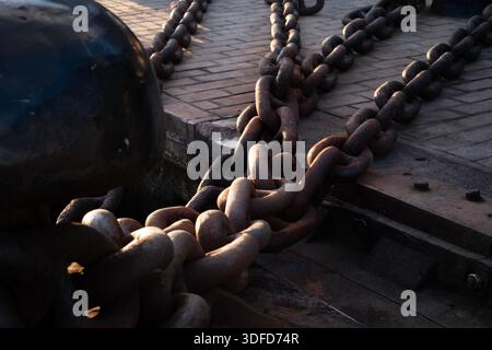 Heavy rusty mooring chains securing large ships to a robust bollard, symbolizing strength, connection, and marine industry on a harbor dock Stock Photo
