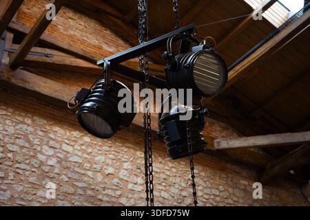 Decorative industrial spotlights hanging from chains, lighting an old stone wall with warm light in a rustic interior Stock Photo