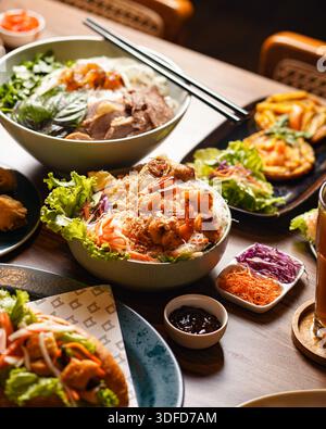 Variety of Vietnamese food served on a table including rice bowls, spring rolls and condiments Stock Photo