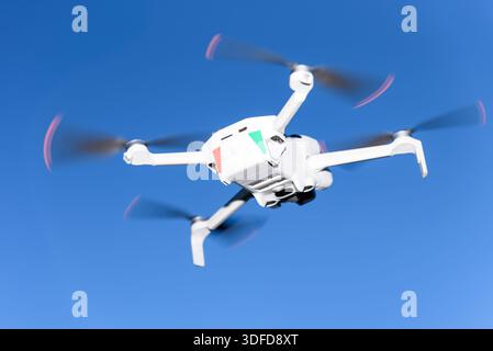Flying drone in clear blue sky, modern unmanned aerial vehicle in flight. Concept of aerial photography, technology, innovation, robotics, and future Stock Photo