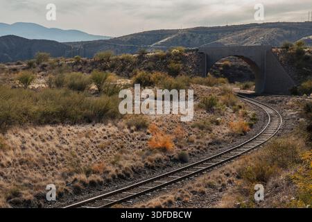 Curved train track going through distant tunnel in desert landscape Stock Photo