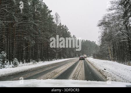 Russia, Saint Petersburg, 11.01.2026 Dirty winter road with cars driving through snow and dense forest. View from inside a car on a dangerous snowy hi Stock Photo