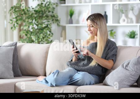 Blonde woman using smart phone sitting on a couch at home Stock Photo