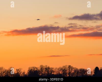 Airplane flying through dramatic orange sunset sky Stock Photo