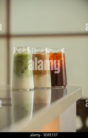 Three iced beverages served in clear glasses on a clean, minimal studio background, including a matcha latte, an iced coffee and coffee latte. Stock Photo