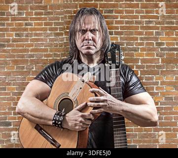 The rocker with a broken guitar on background of the brick wall. Guitarist on acoustic guitar Stock Photo