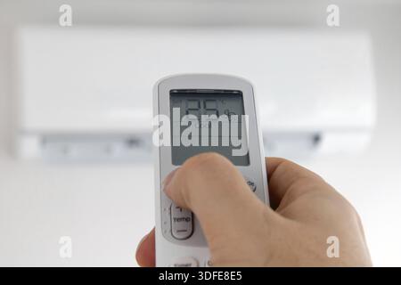 Hand with remote control directed on air conditioner. Air conditioner inside the room with man operating remote controller Stock Photo