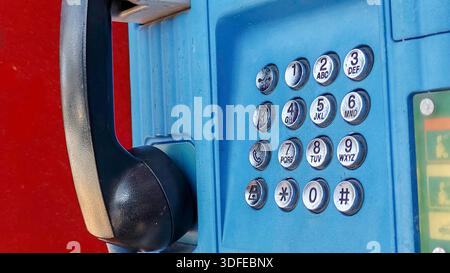 Blue Public Telephone Station with Black Handset and Keypad Against a Red Background Stock Photo