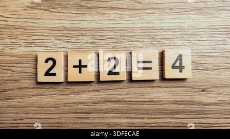 Simple addition math equation two plus two equals four using wooden number tiles on wood background Stock Photo