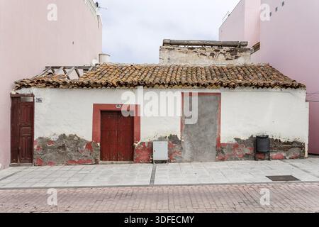 An old, weathered building with a tiled roof, red doors, and peeling walls Stock Photo
