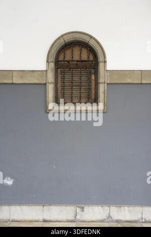 Arched window with wooden shutter on two-toned wall Stock Photo