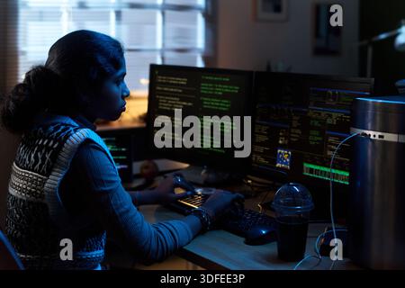 Young Indian Woman Coding on Computer Monitors in Dark Home Office Stock Photo