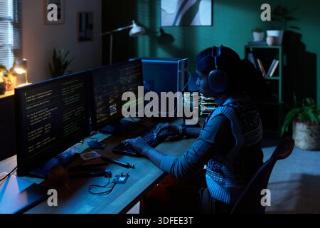 Young Woman Coding Software on Multiple Computer Monitors at Night Stock Photo