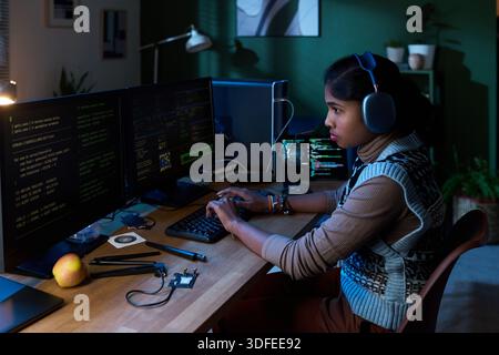 Young South Asian Woman Coding Software on Computer Monitors at Night Stock Photo