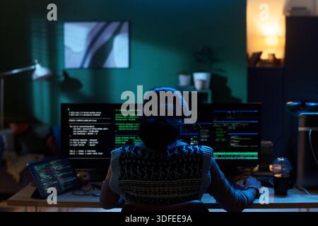 Young Woman Coding on Computer Monitors in Dark Home Office Setting Stock Photo