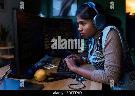 Young South Asian Woman Coding on Computer While Wearing Headphones Stock Photo