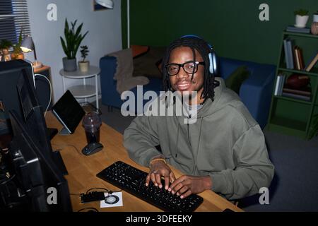 Portrait of Young Black Man Wearing Headphones Using Computer at Desk Stock Photo