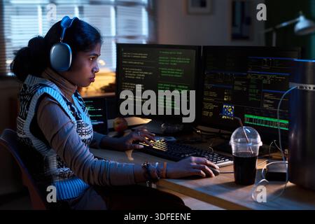 Young South Asian Woman Coding on Multiple Monitors at Night in Office Stock Photo