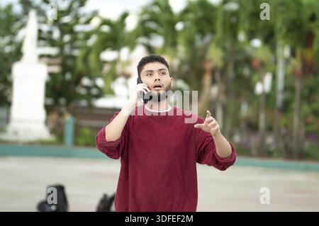 Young man talking on the phone and gesturing outdoors. White man talking on cell phone in the park Stock Photo