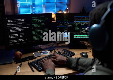 Young Black Man Coding Software on Computer Monitors at Night Stock Photo