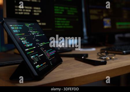 Tablet Displaying Programming Code on Desk with Computer Monitors in Background Stock Photo