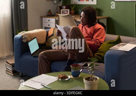 Young Black Man Reviewing Documents While Sitting on Sofa at Home Stock Photo