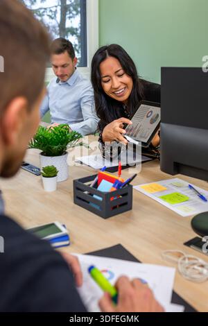 Portrait of smiling hispanic businesswoman discussing charts on tablet during office meeting Stock Photo