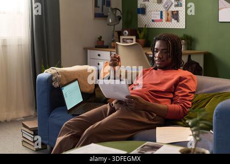 Young Black Man Reviewing Documents While Working Remotely from Home Stock Photo