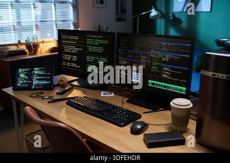 Empty Office Desk Displaying Multiple Computer Screens Running Programming Code Stock Photo