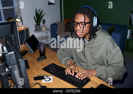 Young Black Man Wearing Headphones Using Computer While Working Stock Photo