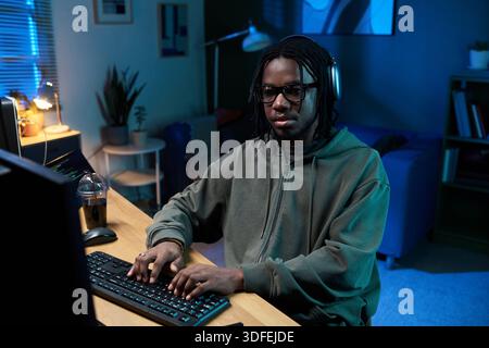 Young Black Man Wearing Headphones Working on Computer at Night Stock Photo